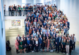 Group photo of the approx. 200 participants of the IDOS anniversary event in the Bundeskunsthalle in Bonn positioned on a large staircase.