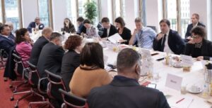 Eine Gruppe von Personen sitzt um einen langen Konferenztisch während der Veranstalltung