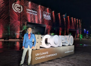 IDOS Researcher Niklas Wagner  in front of a large illuminated COP30 installation at the conference venue in Belém, Brazil. The UN Climate Change Conference building is lit up in the background at night.
