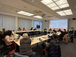 Photo: Internationale Journalist*innen bei Ihrem Stopp im IDOS, während eine Präsentation im Veranstaltungssaal gehalten wird.