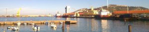 Harbor in Ceuta with boats, docked ships, waterfront buildings, and surrounding hills.