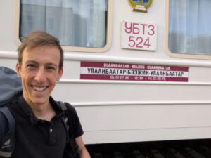Photo: IDOS researcher Niklas Wagner smiling in front of a train from Ulanbaatar to Beijing.